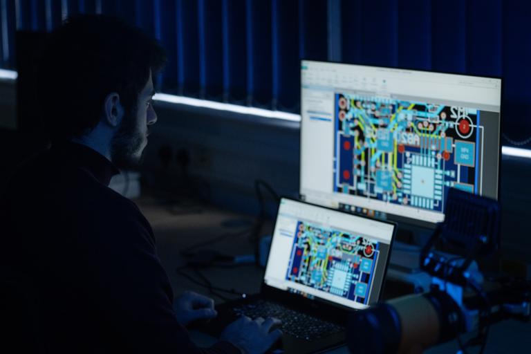 A male sitting in the dark looking at a computer screen filled with complex diagrams and processes